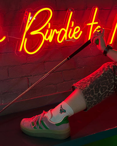 Person wearing wee birdie socks with a neon sign in the background