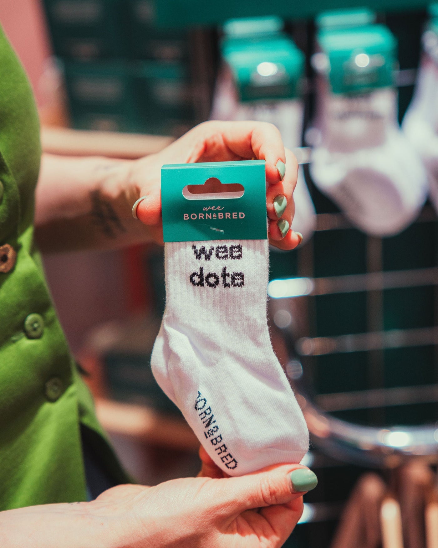 Person holding white baby socks with wee dote text on them