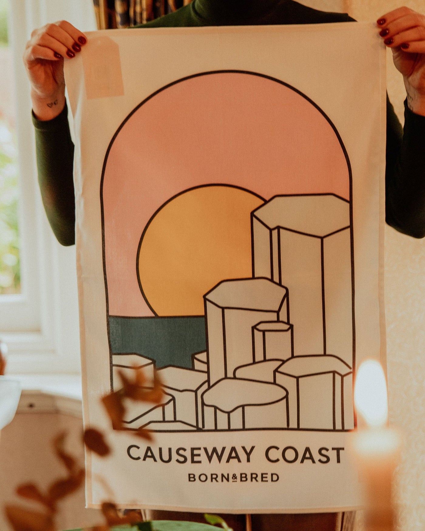 Person holding a poster of the Causeway Coast design with a sunset and geometric shapes.