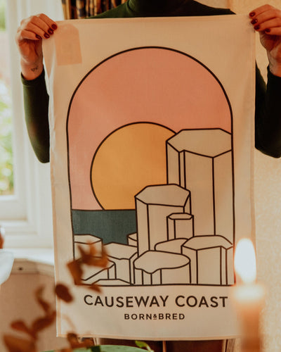Person holding a poster of the Causeway Coast design with a sunset and geometric shapes.